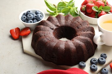 Tasty chocolate bundt cake, tea and berries on light table, closeup