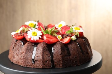 Delicious chocolate bundt cake with strawberries, chamomile flowers and mint on stand against blurred beige background, closeup