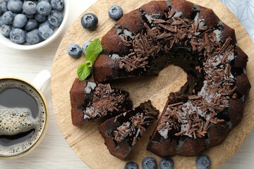 Delicious bundt cake with blueberries, mint, chocolate shavings and coffee on light wooden table, flat lay