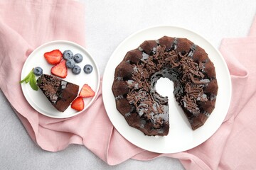 Delicious chocolate bundt cake with strawberries and blueberries on light grey textured table, flat...