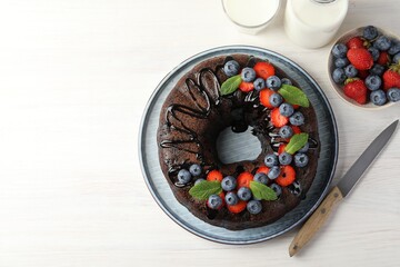 Delicious chocolate bundt cake with strawberries, mint and blueberries on light wooden table, flat...