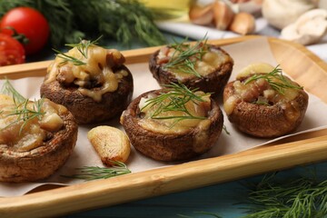 Delicious stuffed mushrooms with melted cheese, garlic and dill on light blue wooden table, closeup