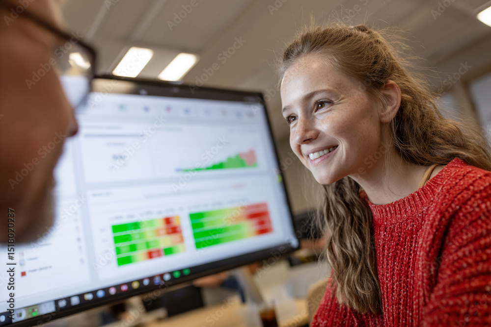 Poster woman in red sweater looks at computer screen displaying data graphs, conveying collaboration and da