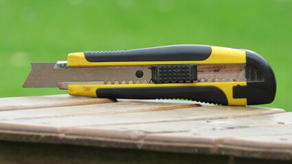 Utility knife rests on a wooden surface in a green garden during daylight