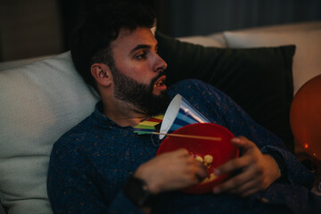 A man unwinding on a couch while holding a snack bowl, amidst party items. His casual mood reflects...