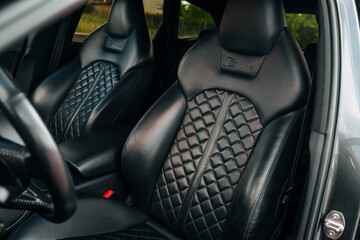 Sports car interior. Black premium leather, bucket seats, steering wheel, buttons, console with gears and widescreen. Luxury car interior design. Marketing, advertising or press articles.