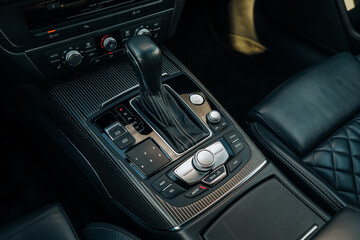 Obraz premium The photo shows the center console, buttons and the automatic sports transmission lever. Black premium leather, steering wheel. Luxury car interior design. Marketing, advertising or press articles.