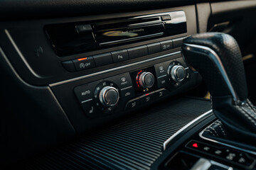 The photo shows the center console, buttons and control panel for the blower and air conditioning. Black premium leather. Luxury interior design of the car. Marketing, advertising or press articles.