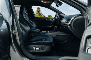 Sports car interior. Black premium leather, bucket seats, steering wheel, buttons, console with gears and widescreen. Luxury car interior design. Marketing, advertising or press articles.