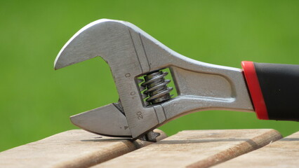 Adjustable wrench resting on wooden surface during bright daylight in a garden setting