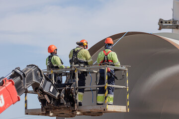 Construction workers wearing safety gear on an aerial lift platform at an industrial building site.