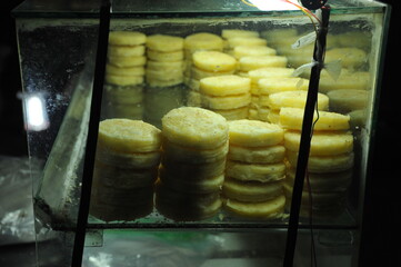 stacks of yellow rice cakes displayed in a glass container of street food vendor in Hue, Vietnam.