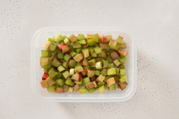 Freshly chopped green rhubarb prepared in plastic box ready for frozen on white background. Trendy...