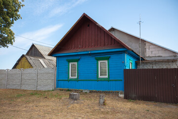 Bright blue wooden house stands in a quiet rural area with painted details and neighboring structures on a sunny day