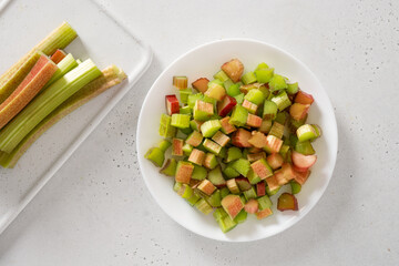 Freshly chopped rhubarb in white plate on white background. Trendy organic food. Ready for cooking. Vegan concept. View from above.