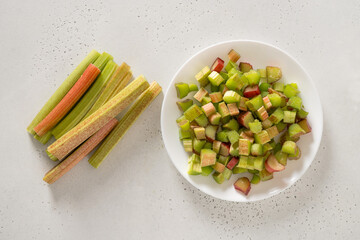 Freshly chopped rhubarb in white plate on white background. Trendy organic food. Ready for cooking. Vegan concept. View from above.