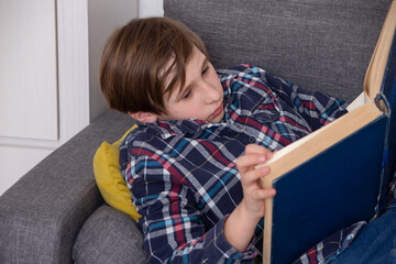 Young boy engrossed in reading a book on a gray couch