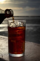 Pouring cola drink on glass with ice cubes