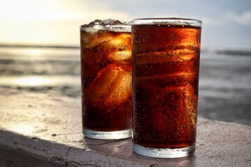 Cola drink with ice cubes and beach with blue sky