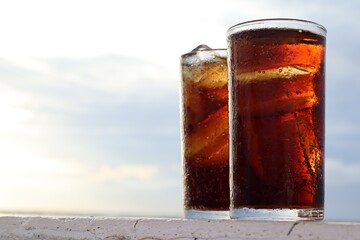 Cola drink with ice cubes and beach with blue sky