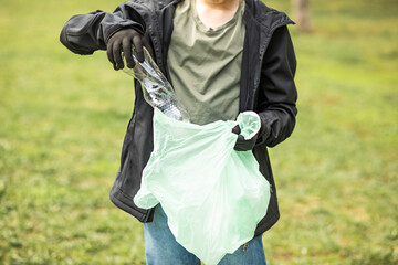 Teenager kid boy picking up trash plastic bottles in the park. Volunteer concept. Ecology,...