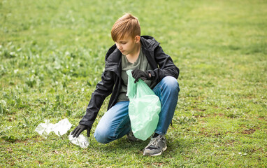 Teenager kid boy picking up trash plastic bottles in the park. Volunteer concept. Ecology,...
