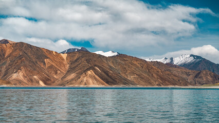 Obraz premium Scenic view of Pangong Lake surrounded by majestic brown mountains under a clear blue sky, reflecting pristine waters, creating a serene and picturesque high-altitude Himalayan landscape in Ladakh