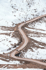 A winding road climbs through the rugged snowy slopes of Ladakh high-altitude mountains, capturing the breathtaking elevation, and dramatic terrain of India trans-Himalayan adventure route