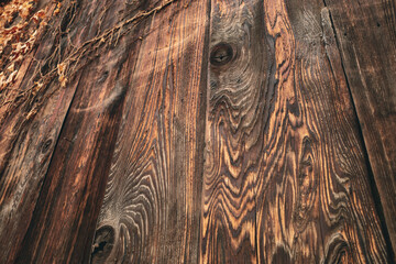 An weathered wooden planks with a rich, dark brown color. The wood grain is highly visible and forms intricate, wavy patterns.