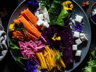 Colorful fresh vegetable salad platter with shredded carrots, purple cabbage, cucumber, red bell pepper, coconut, and garnished with edible flowers on a bed of green lettuce