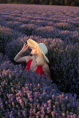 Beautiful girl in red dress and hat in lavender field in summer at sunset