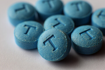 pile of blue pressed pills with T embossed on each, testosterone themes