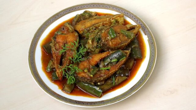 Delicious brinjal (eggplant) curry with hilsa fish on ceramic plate, light wooden surface. Tasty Bengali dish.