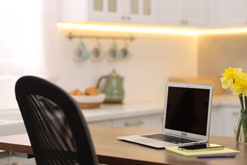Laptop with blank screen, smartphone, stationery and flowers on wooden table in kitchen. Mockup for design