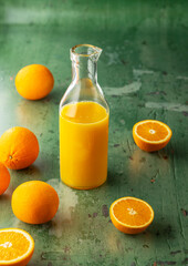 Refreshing orange juice in glass bottle surrounded by oranges on green background