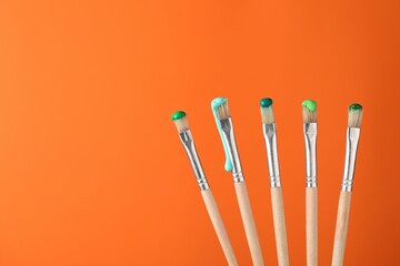 Many brushes with color paints on orange background, closeup. Space for text