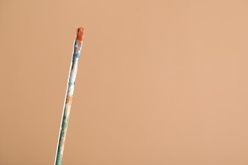 Dirty paintbrush on light brown background, closeup. Space for text