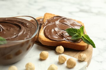 Tasty chocolate spread with mint and hazelnuts on white marble table, closeup
