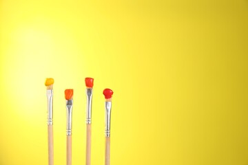 Many brushes with color paints on yellow background, closeup. Space for text