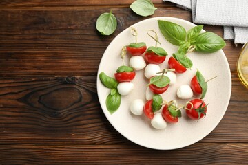 Appetizers with mozzarella, tomatoes and basil on wooden table, flat lay. Space for text