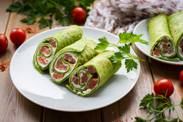 Delicious breakfast: thin spinach pancakes with red fish. Green thin pancakes. Rolls with red fish. Close-up