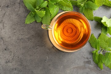 Aromatic lemon balm tea in glass cup and fresh leaves on gray textured table, flat lay. Space for...