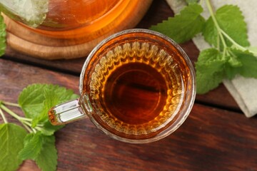Aromatic lemon balm tea in glass cup, teapot and fresh leaves on wooden table, flat lay