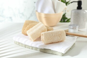 Different loofah sponges and towels on white table, closeup