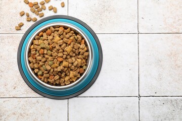 Dry pet food in feeding bowl on light tiled background, top view. Space for text