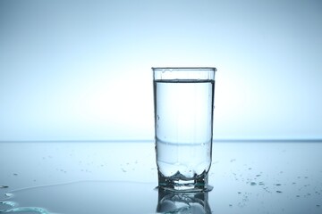 Fresh water in glass on mirror table against light blue gradient background