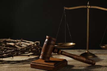 Judge's gavel, scales and crown of thorns on wooden table against black background, closeup