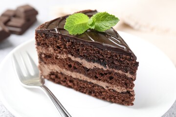 Piece of delicious chocolate cake with mint and fork on table, closeup