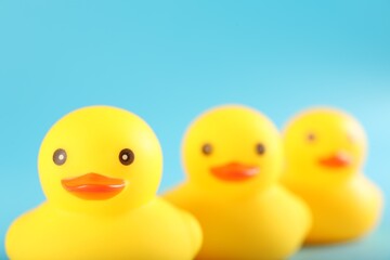 Three cute rubber ducks on light blue background, closeup