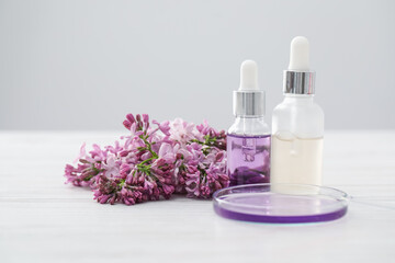 Making luxury perfume. Essential oils in glassware and flowers on white wooden table, closeup